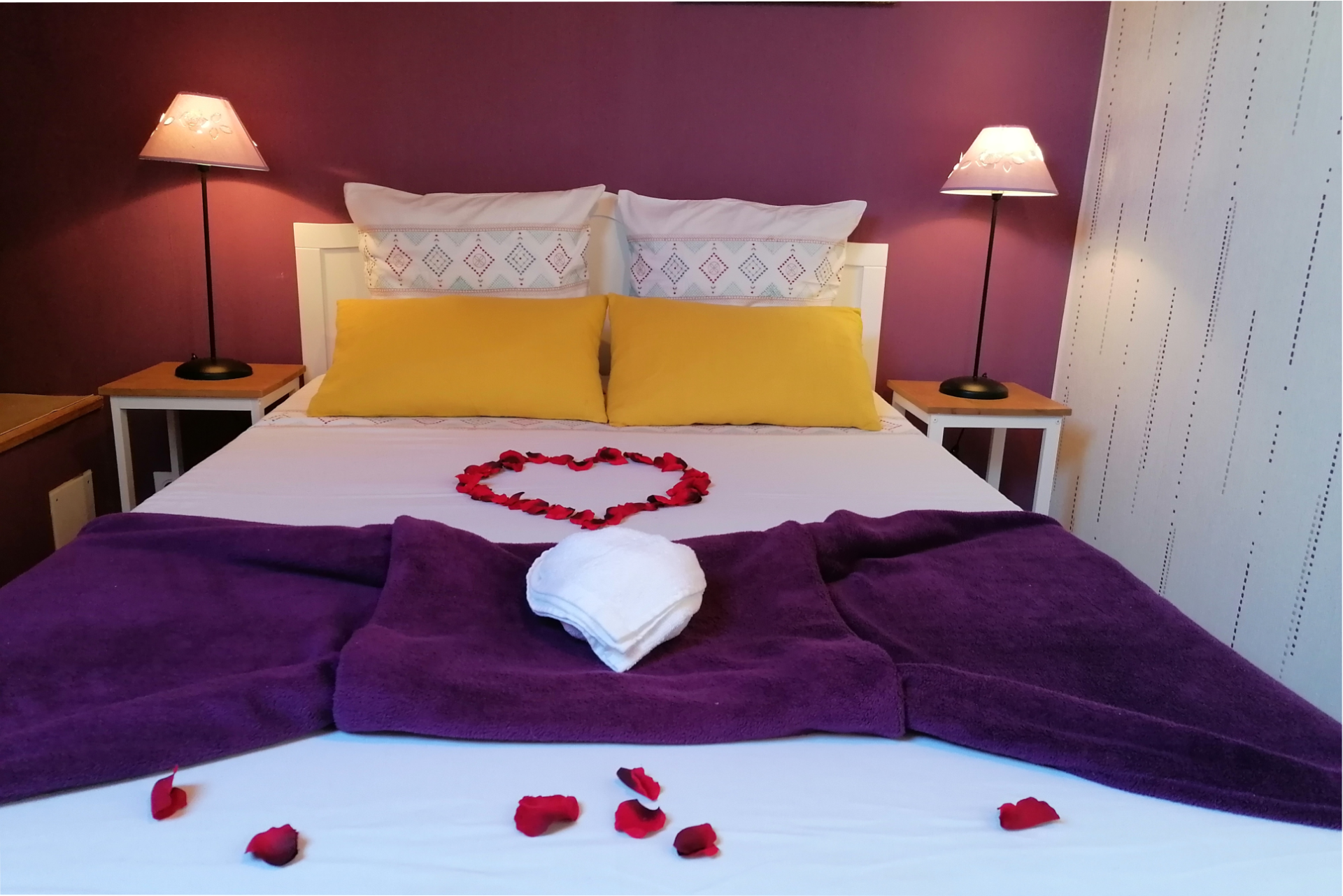 Chambre parentale du gîte décorée pour la Saint-Valentin avec pétales de roses en forme de cœur sur le lit et ambiance romantique.