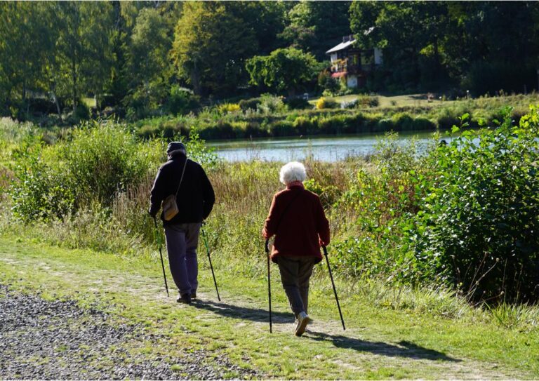 Couple de retraités pratiquant la marche nordique avec bâtons sur un chemin de halage en bord de rivière en Anjou.