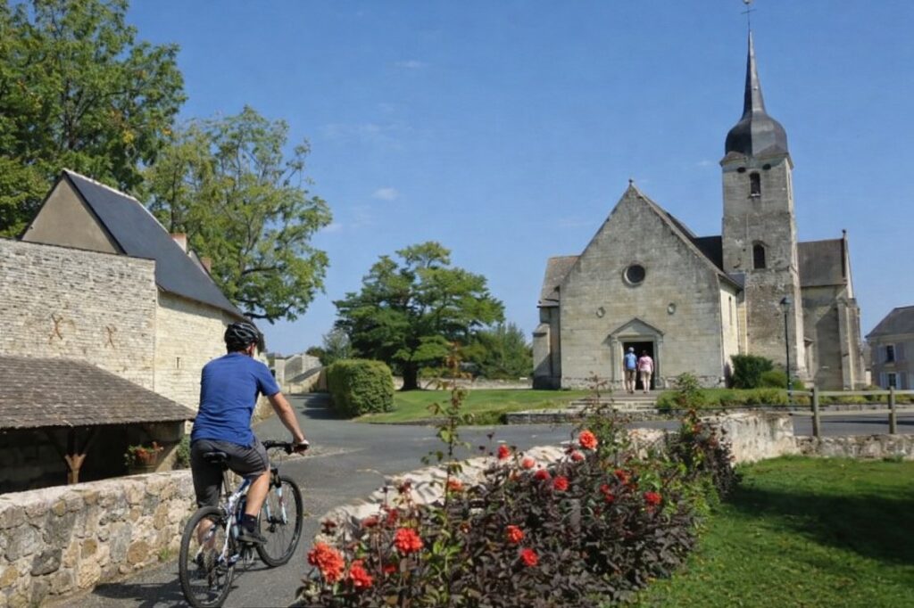Vue panoramique d'un village de charme en Maine-et-Loire avec ses maisons en pierre blanche de tuffeau, ses toits d'ardoise bleue et ses vignes environnantes sous une lumière dorée.
