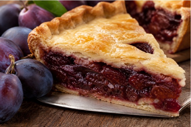 Un pâté aux prunes angevin doré sortant du four, posé sur une table en bois rustique avec un verre de vin blanc Coteaux-du-Layon, illustrant les vieilles recettes de l'Anjou.
