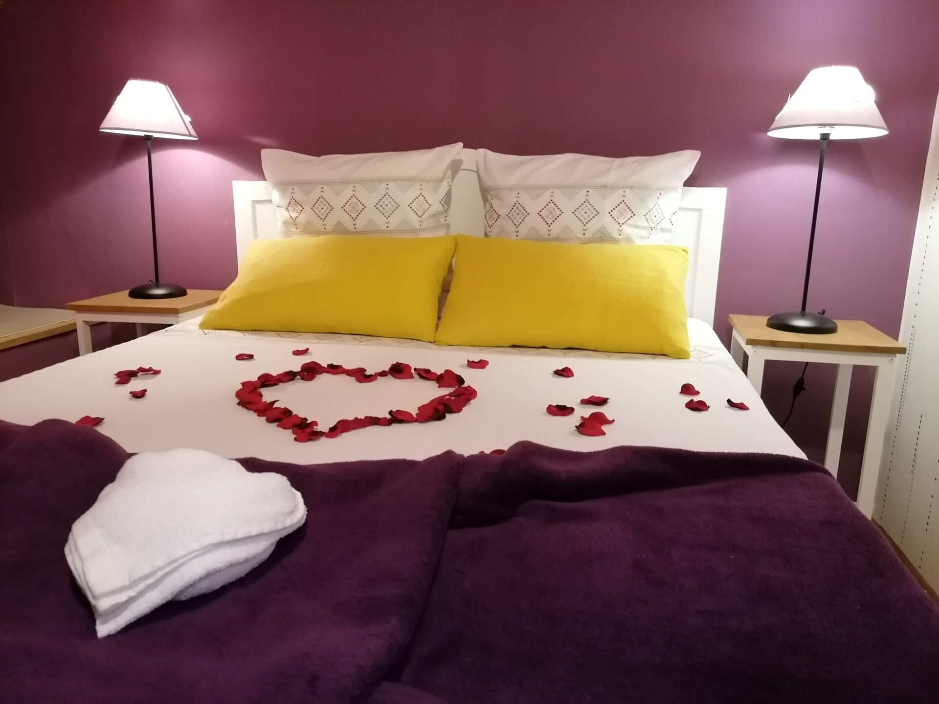 Chambre parentale du gîte décorée pour la Saint-Valentin avec pétales de roses en forme de cœur sur le lit et ambiance romantique.