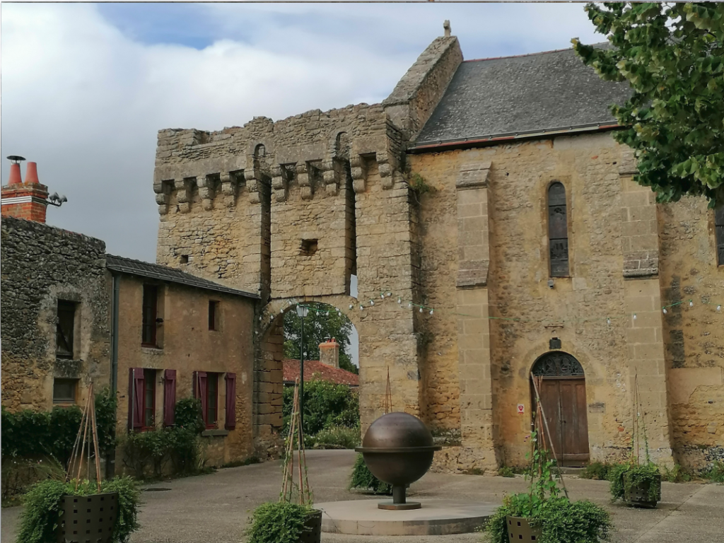 Vue de l'entrée fortifiée du château d'Aubigné-Briand en Maine-et-Loire, présentant une haute porte en pierre de tuffeau et schiste avec des vestiges de pont-levis, jouxtant l'architecture ancienne de l'église communale.